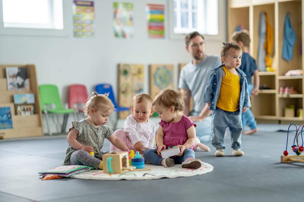 Young children playing together on a playmat in an organized daycare setting with vibrant colors and educational toys. A caregiver provides supervision, fostering a fun and safe learning environment.