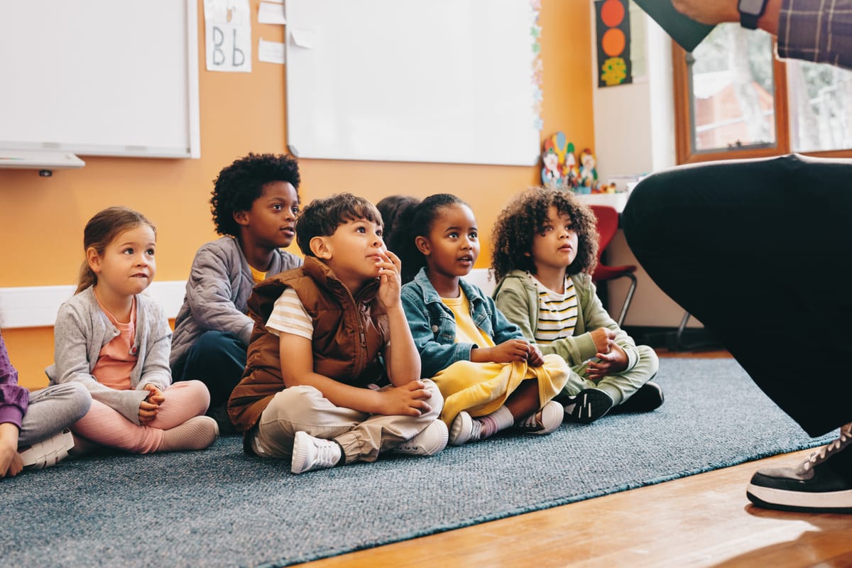 Elementary school students sit and listen to a story from their teacher. Group of young children having a listening comprehension lesson in class. Kids schooling in a multiethnic education centre.