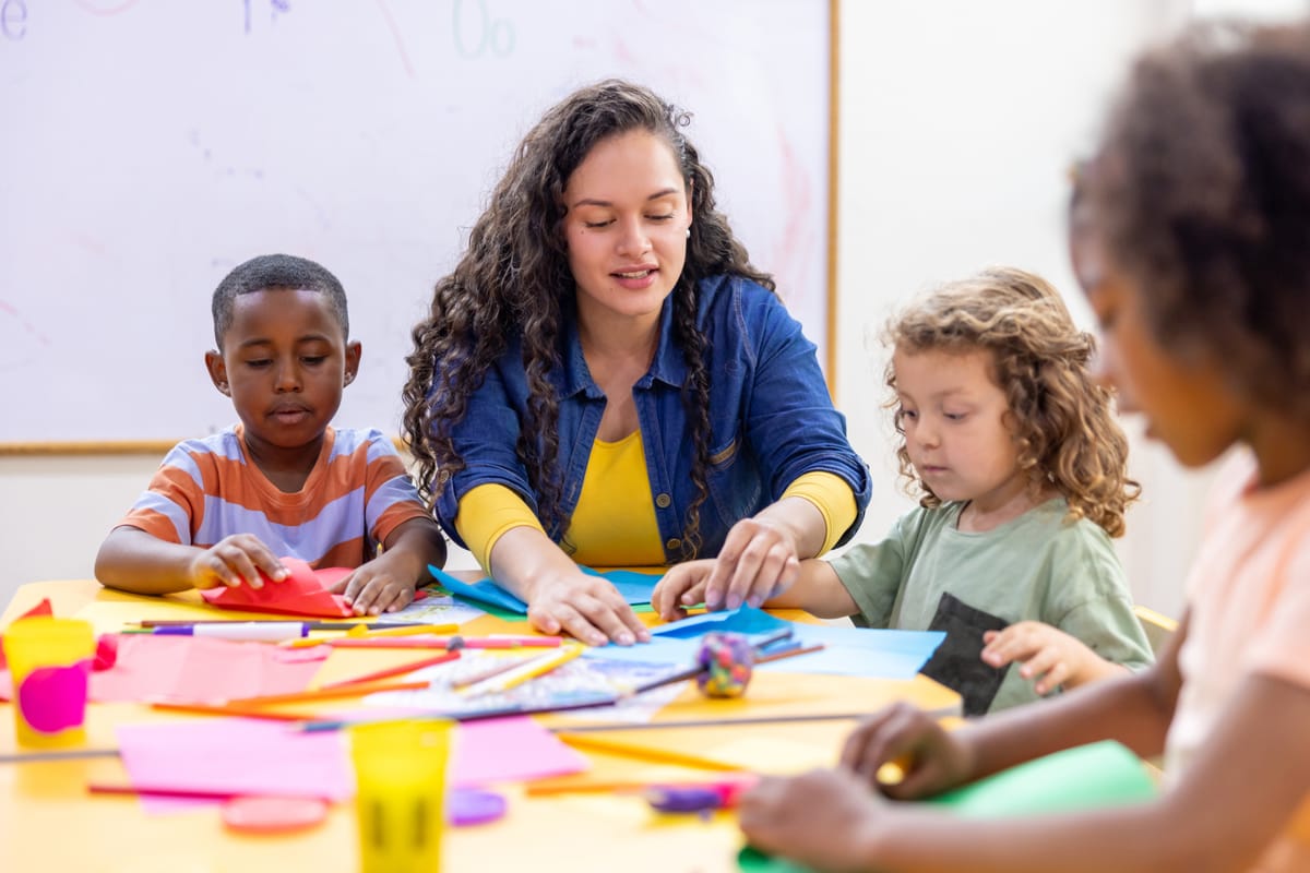 Happy Latin American preschool teacher helping children while doing crafts in class - education concepts