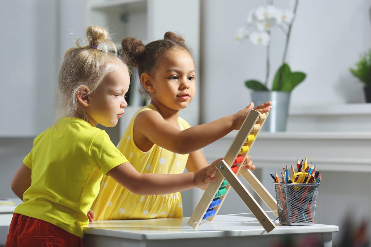 White and Black children sit together at the table and count on the abacus and smiles. Math lesson in elementary school