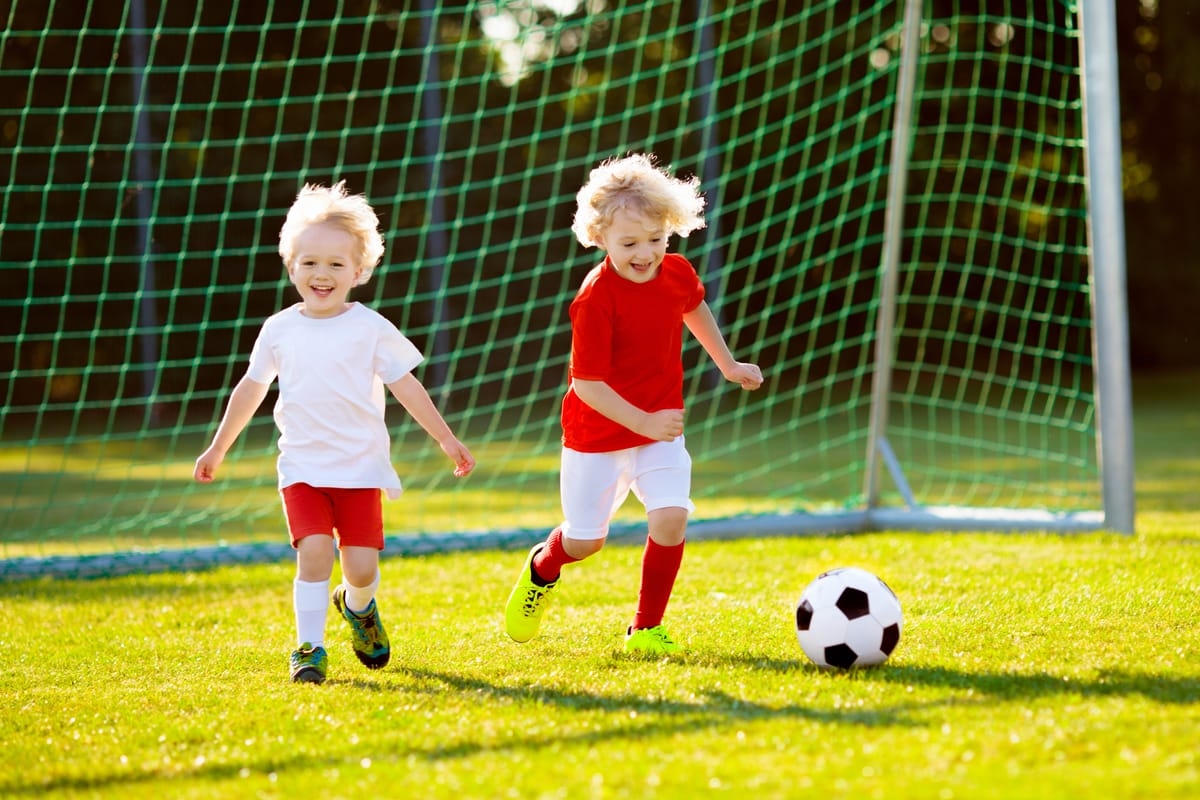 Kids play football on outdoor field. Children score a goal at soccer game. Little boy kicking ball. Running child in team jersey and cleats. School football club. Sports training for young player.