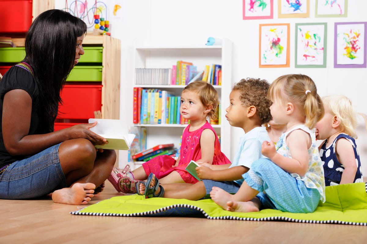 A teacher/carer/ childmider reading to a group of toddlers in a nursery setting.