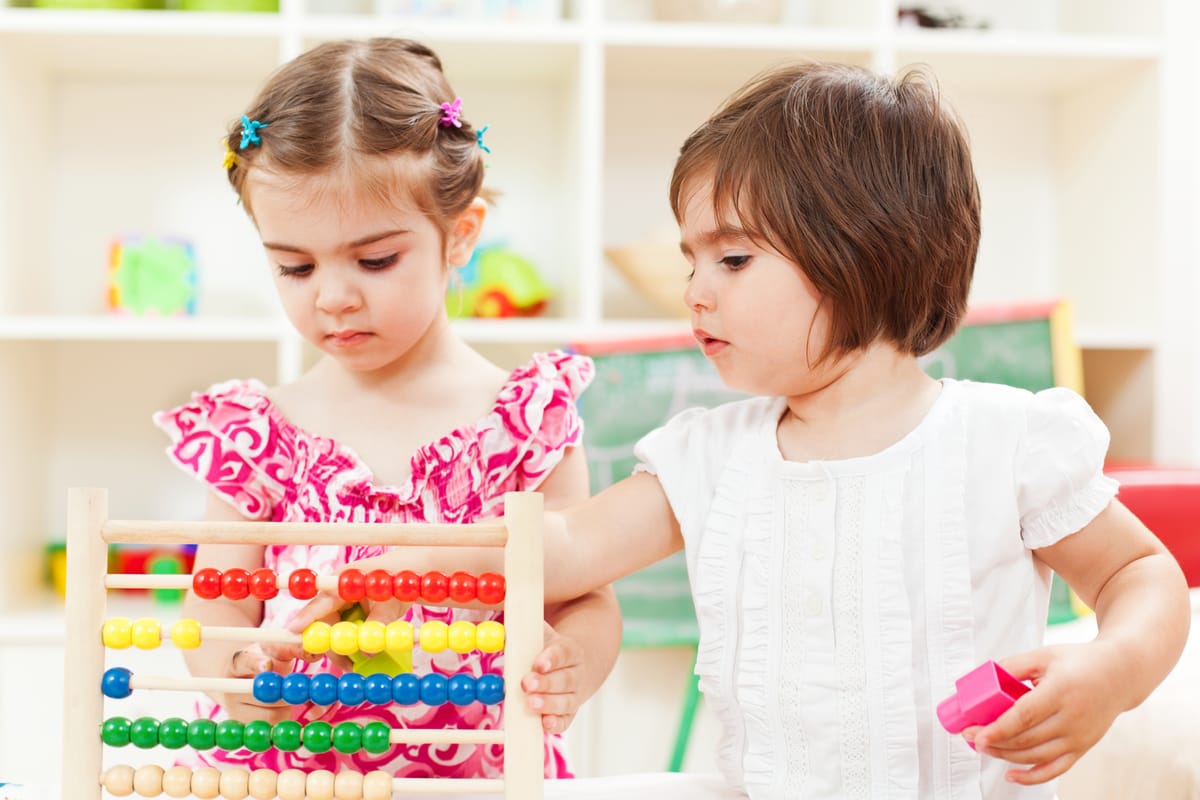 Two preschooler girls learning to count on a wooden abacus